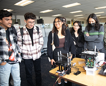 High school students smile as they stand around lab equipment