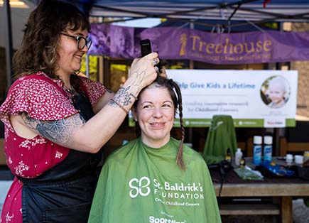 A person smiles while getting their hair shaved off