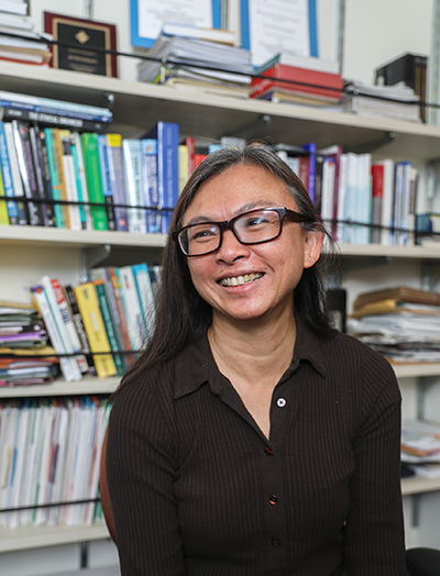 Sri Kurniawan smiles in front of a bookcase filled with books