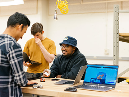 One students smiles while two look at computers