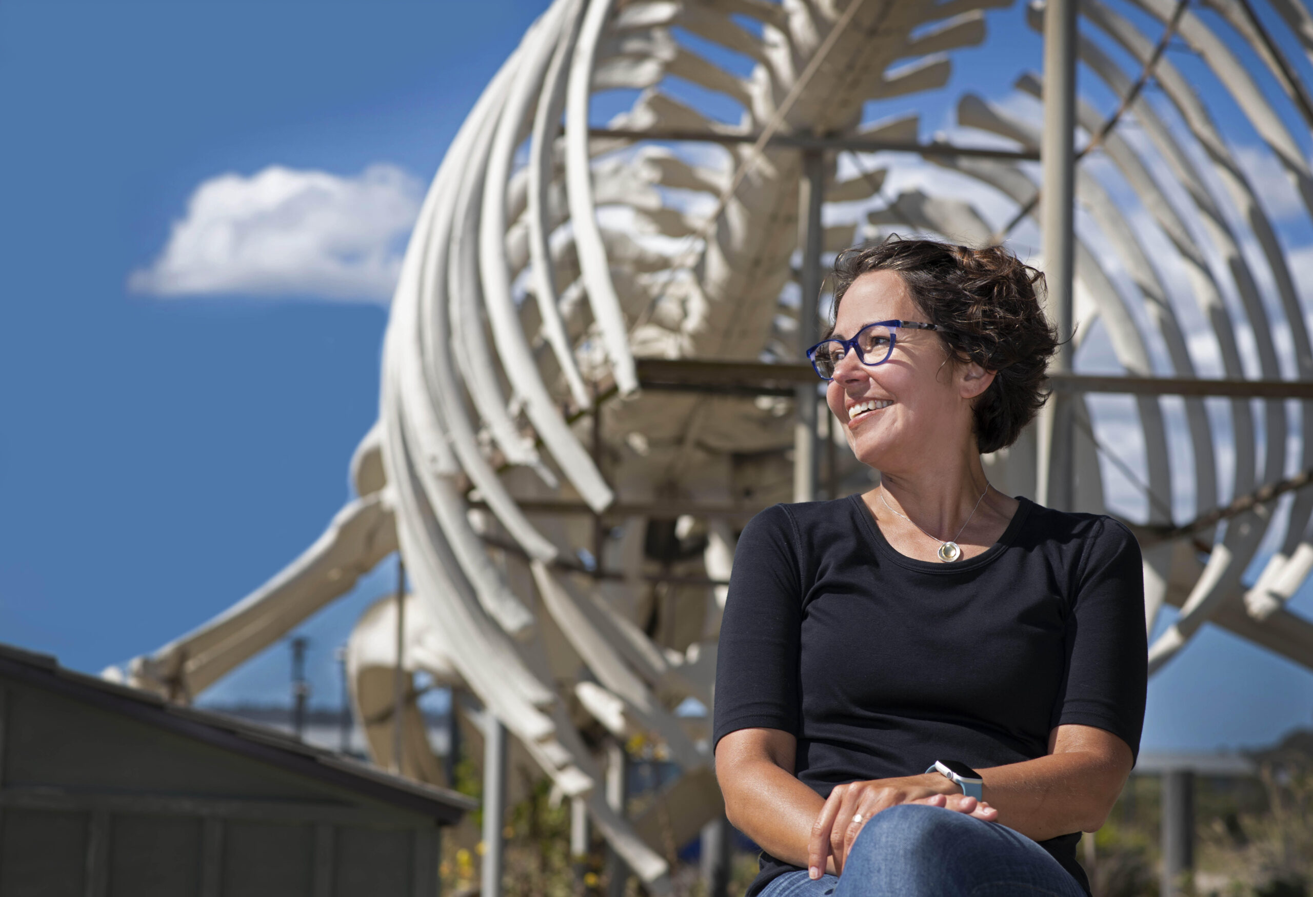 Beth Shapiro sitting in front of blue whale skeleton at Seymour Marine Discovery Center