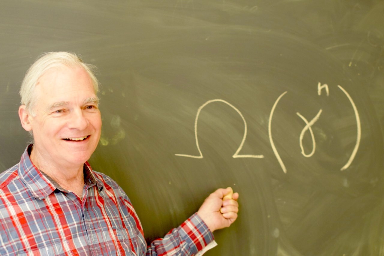 Allen Van Gelder smiles while writing on a chalk board