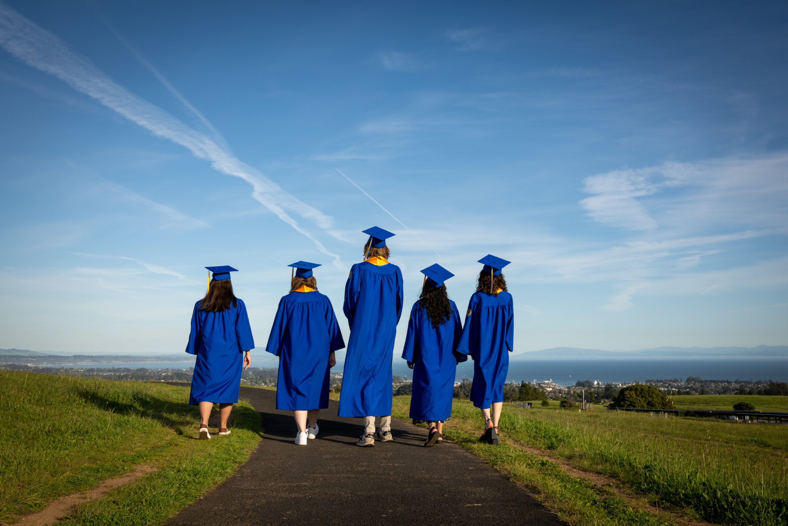 Back profiles of five students in commencement robes on campus