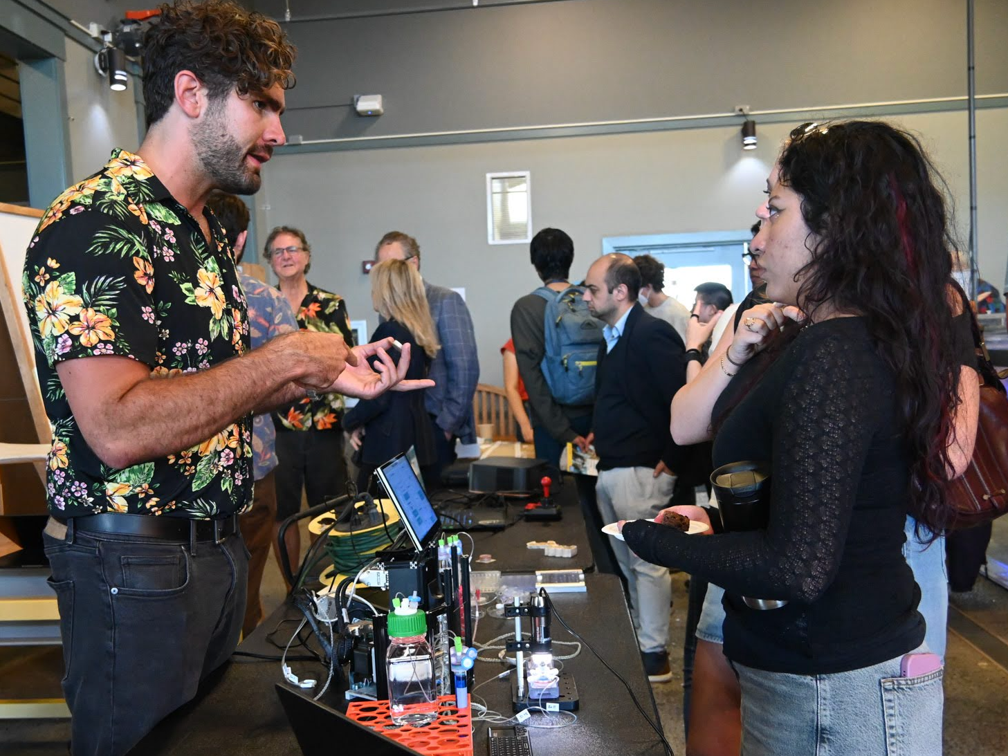 A graduate student speaking with two attendees at a science fair.
