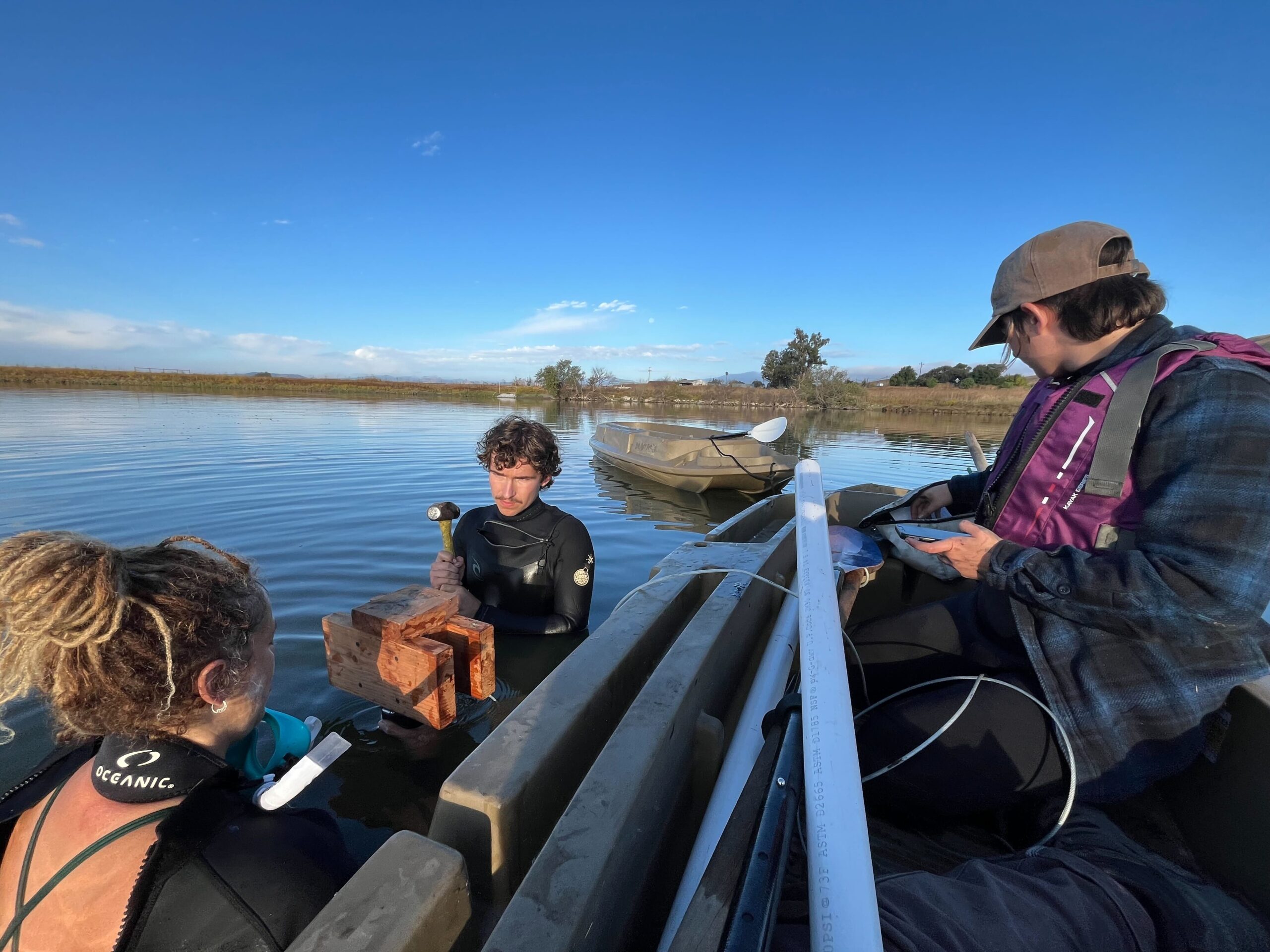 Researchers in wetsuits collecting sediment from a lake