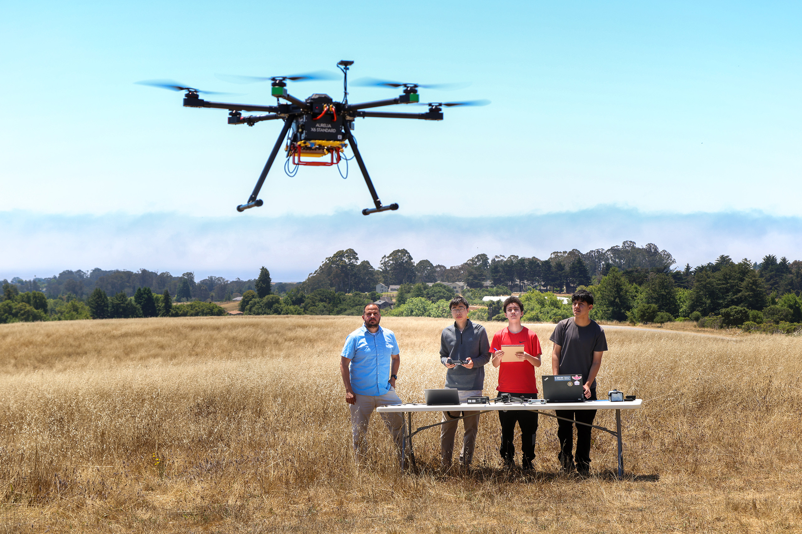 Prof Gonzalez-Rocha and three student look up at a drone flying overhead