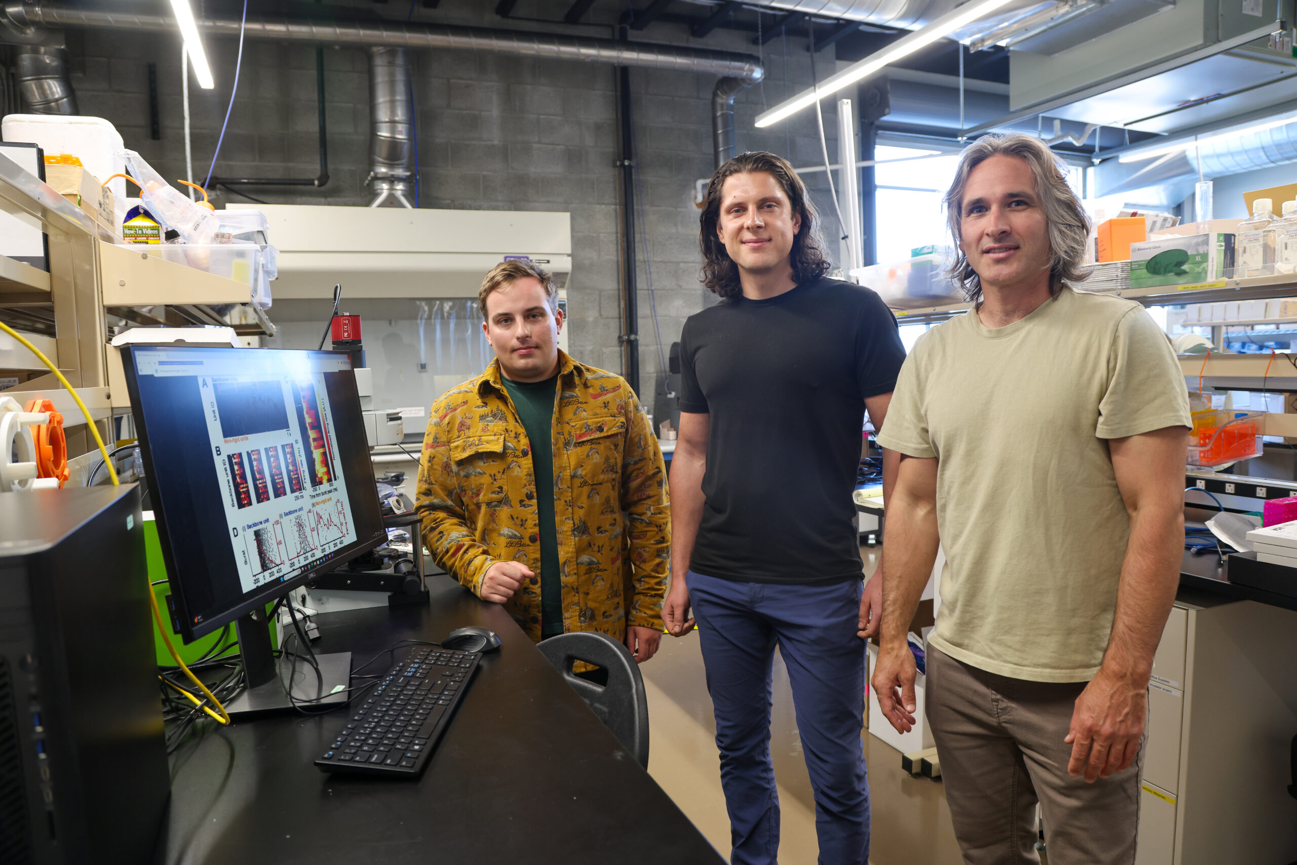 Three researchers smile at the camera in the lab.