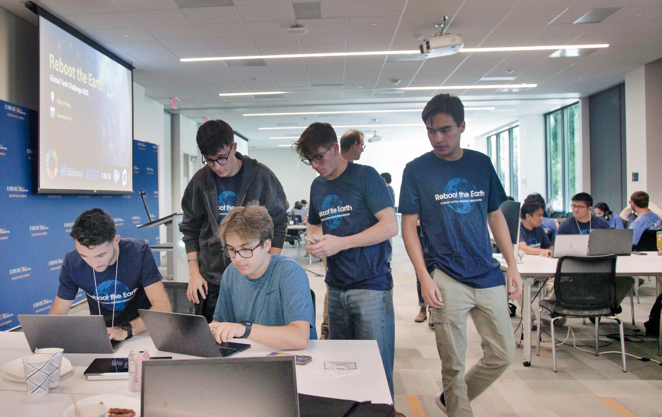 five students wearing 'reboot the earth' t-shirts collaborate around computers