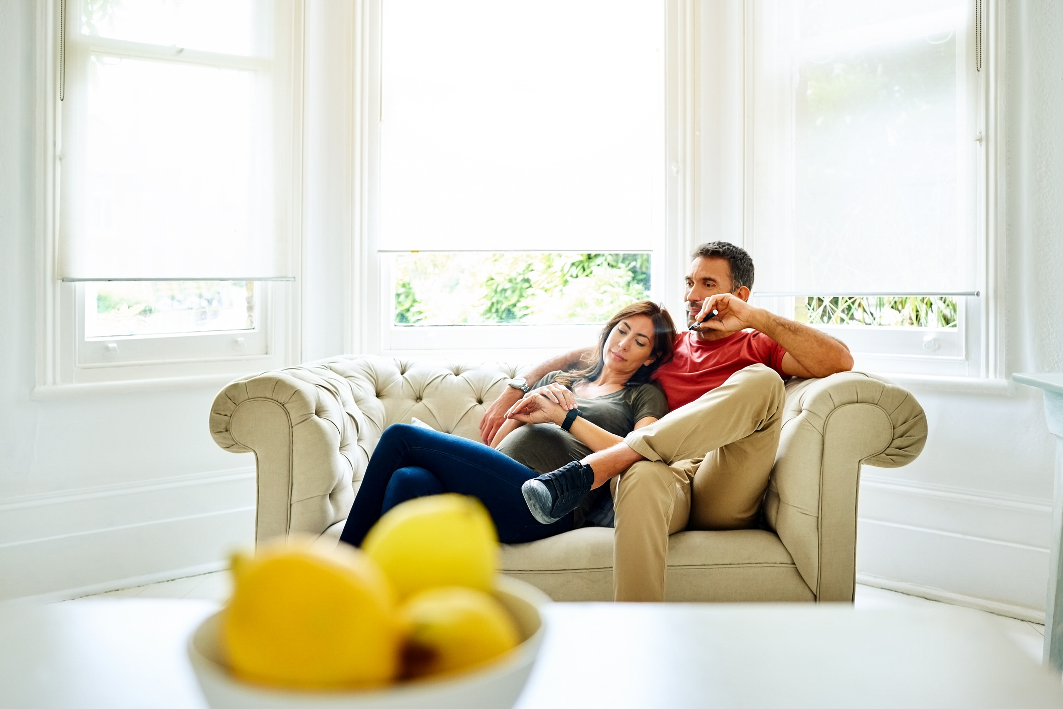 Man holding an e-cigarette while cuddling on couch with pregnant woman
