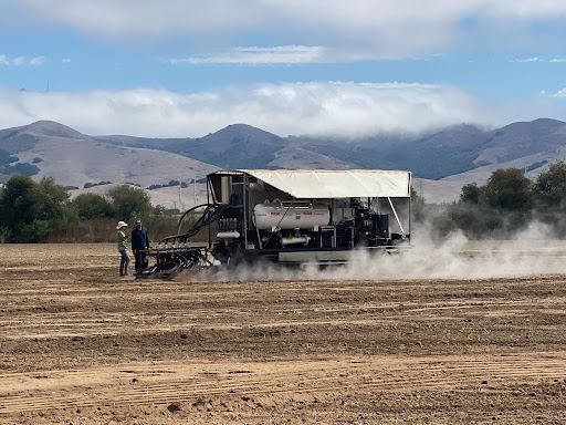A steam injection machine billows steam as it moves across bare farm soil.