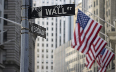 A sign post showing wall street and broad street, with American flags.